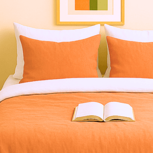 Taies d'oreillers bicolores terre de sienne et blanche assorties à la housse de couette zippée facile à mettre gaze de coton modèle TOSCANE sur lit avec coussins orange et livre ouvert.