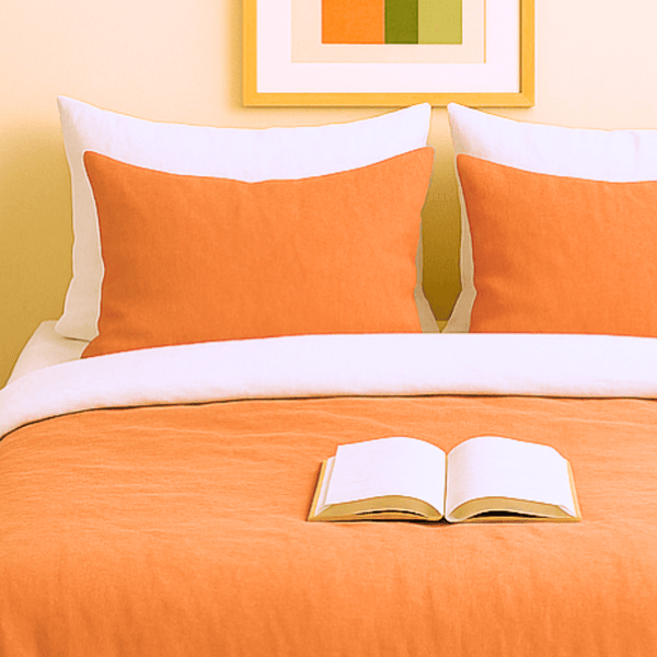 Taies d'oreillers bicolores terre de sienne et blanche assorties à la housse de couette zippée facile à mettre gaze de coton modèle TOSCANE sur lit avec coussins orange et livre ouvert.